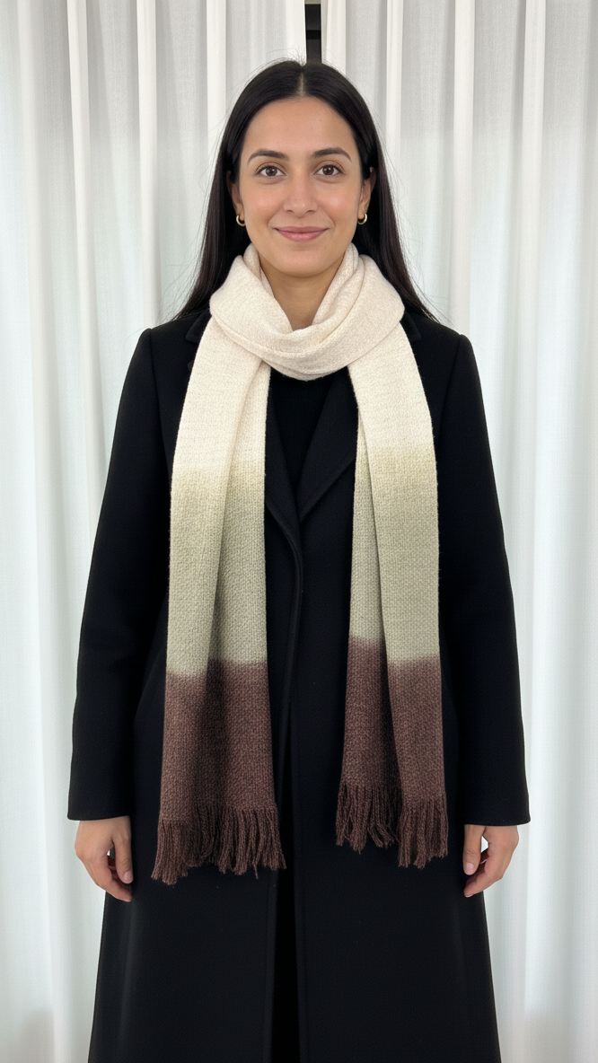 Woman wearing a black coat and a white to brown gradient scarf against a white curtain background