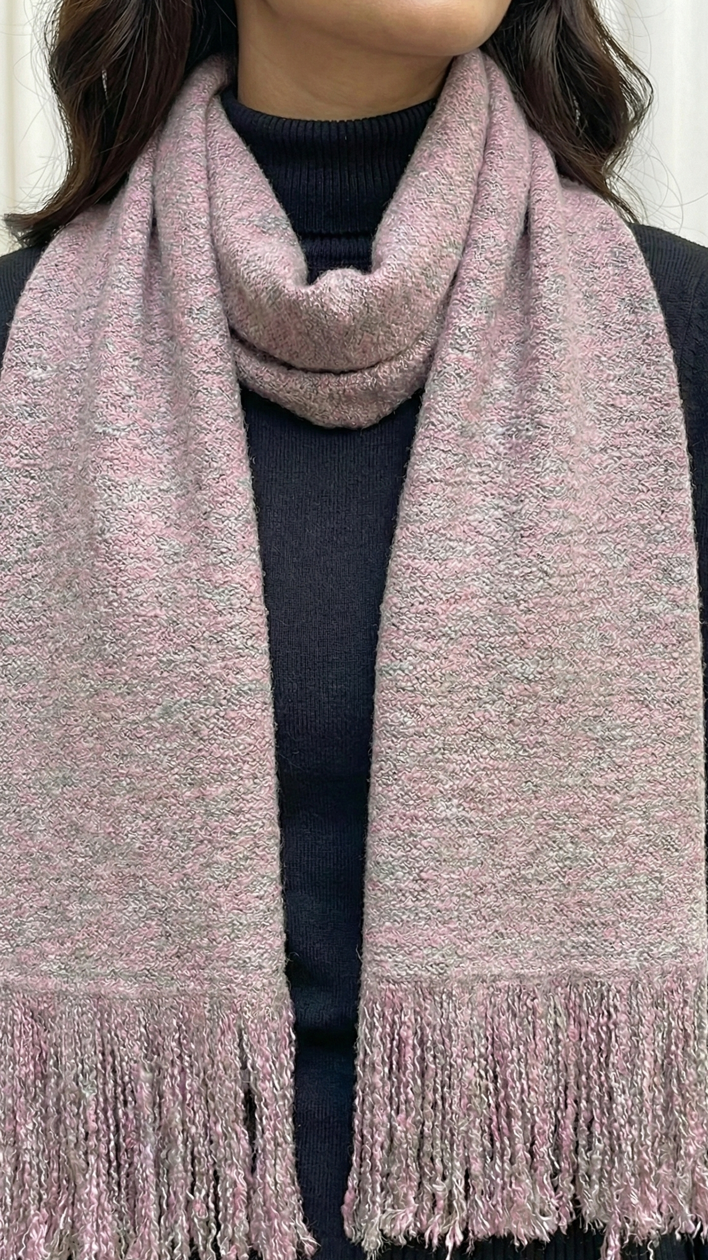Person wearing a pink scarf with fringes on a plain background