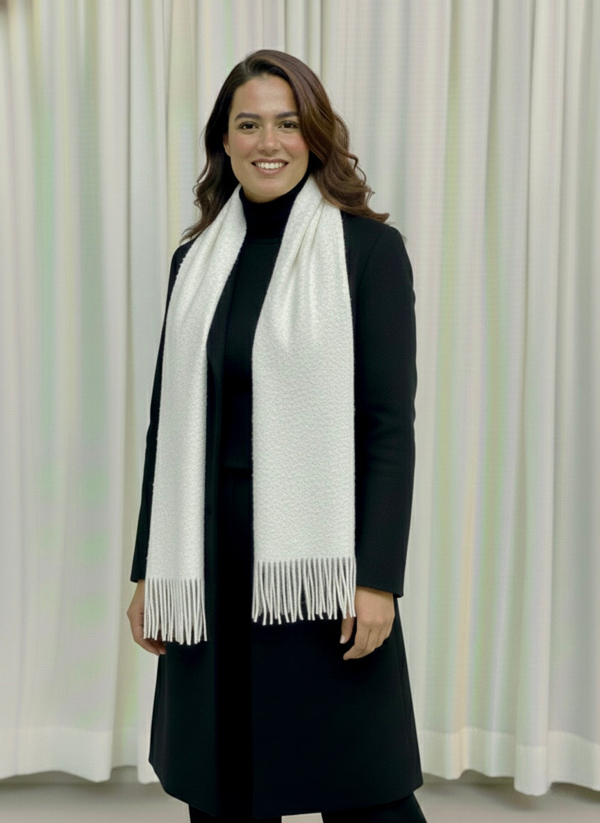 Woman wearing a black coat and white scarf against a light curtain background