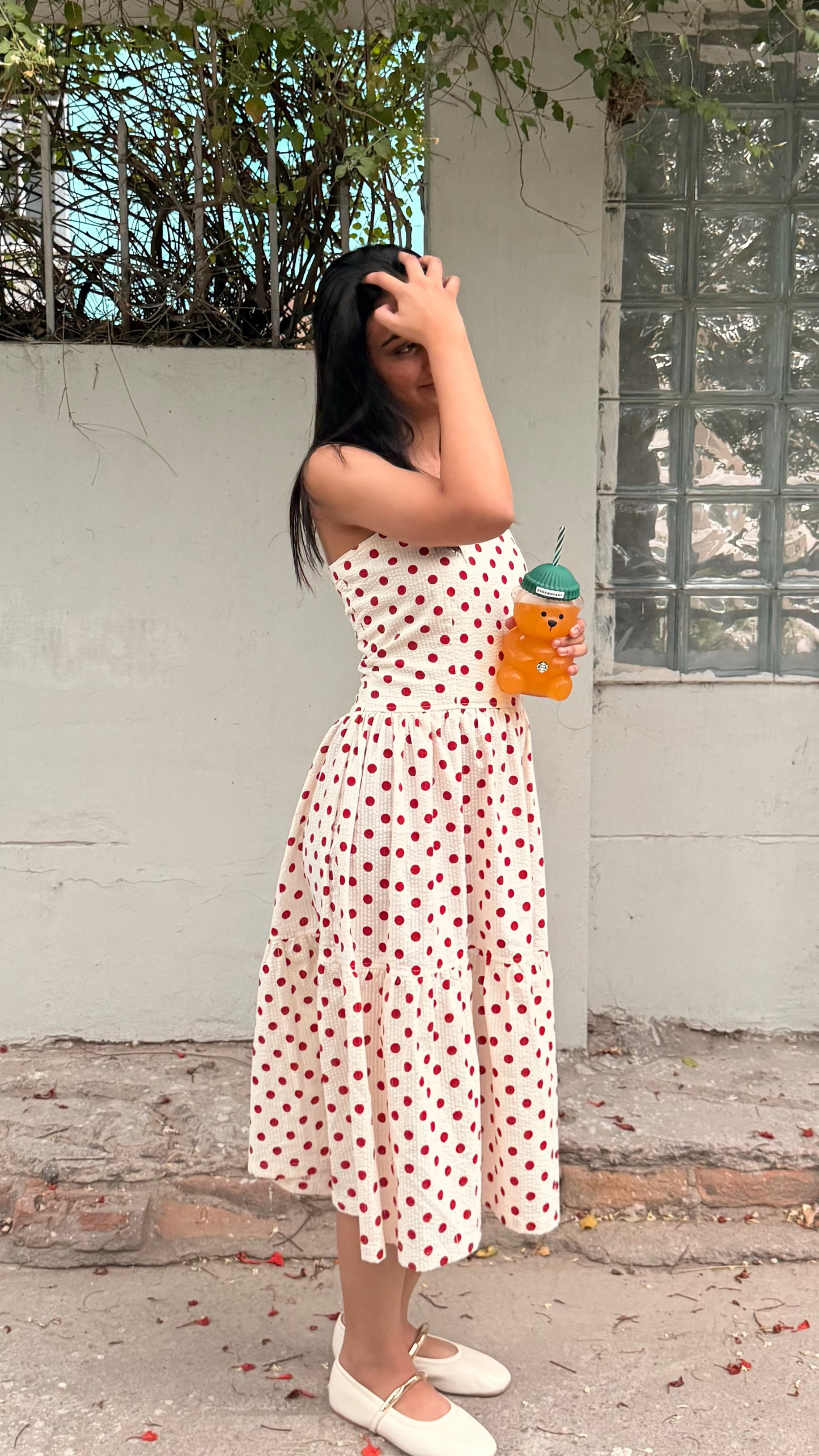 Woman in a white dress with red patterns standing outdoors, holding a drink.