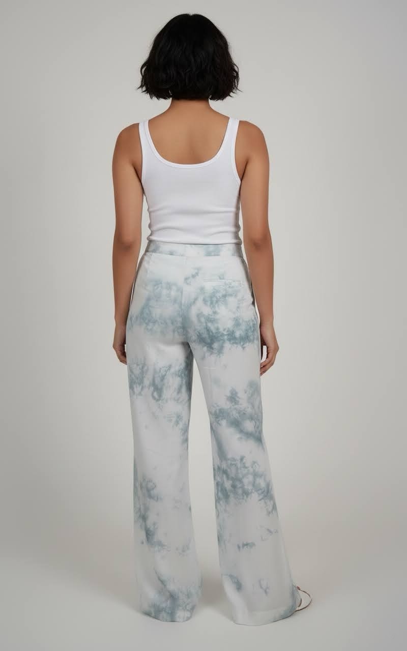 Person wearing a white tank top and light blue tie-dye pants on a plain background