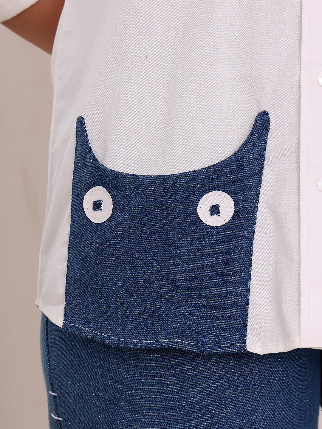 Close-up of a white shirt with blue denim pocket and white buttons on a beige background