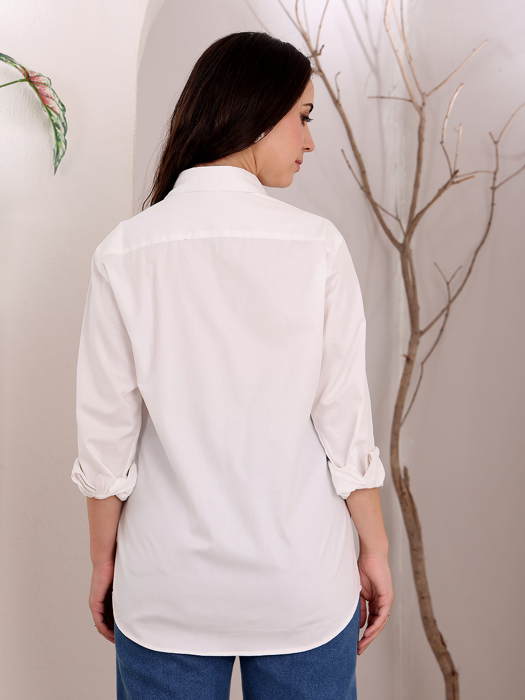 Woman wearing a white shirt and blue jeans against a neutral background