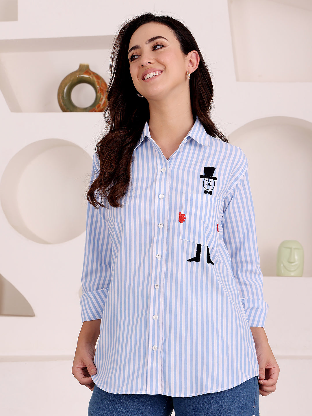 Woman wearing a blue and white striped shirt with a cartoon design, standing in a room with decorative items.