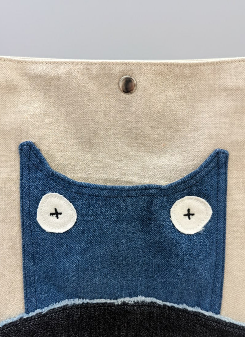 Close-up of a fabric pouch with blue cat face design on beige background