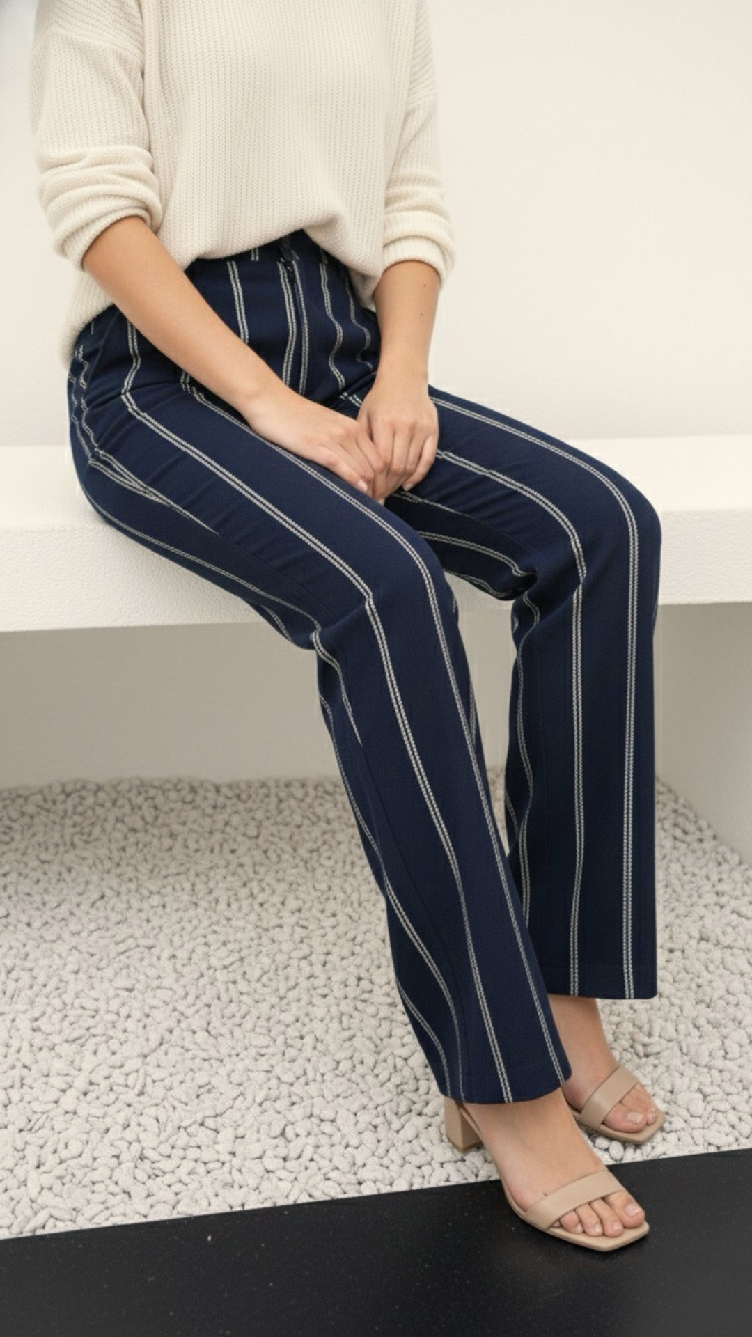 Person wearing navy striped pants sitting on a white surface.