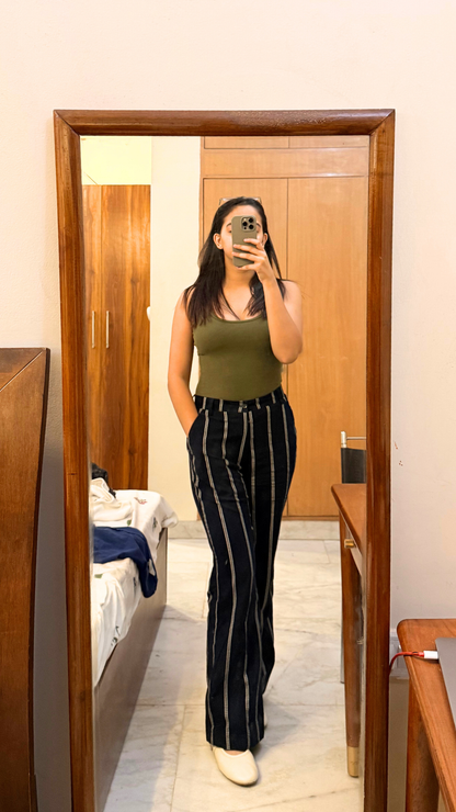 Person taking a mirror selfie wearing a green top and black pants with white stripes.