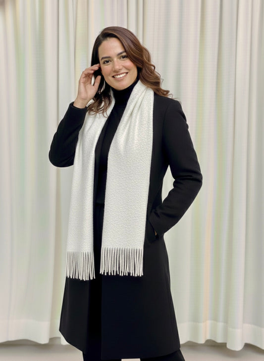 Woman wearing a black coat and white scarf against a white curtain background