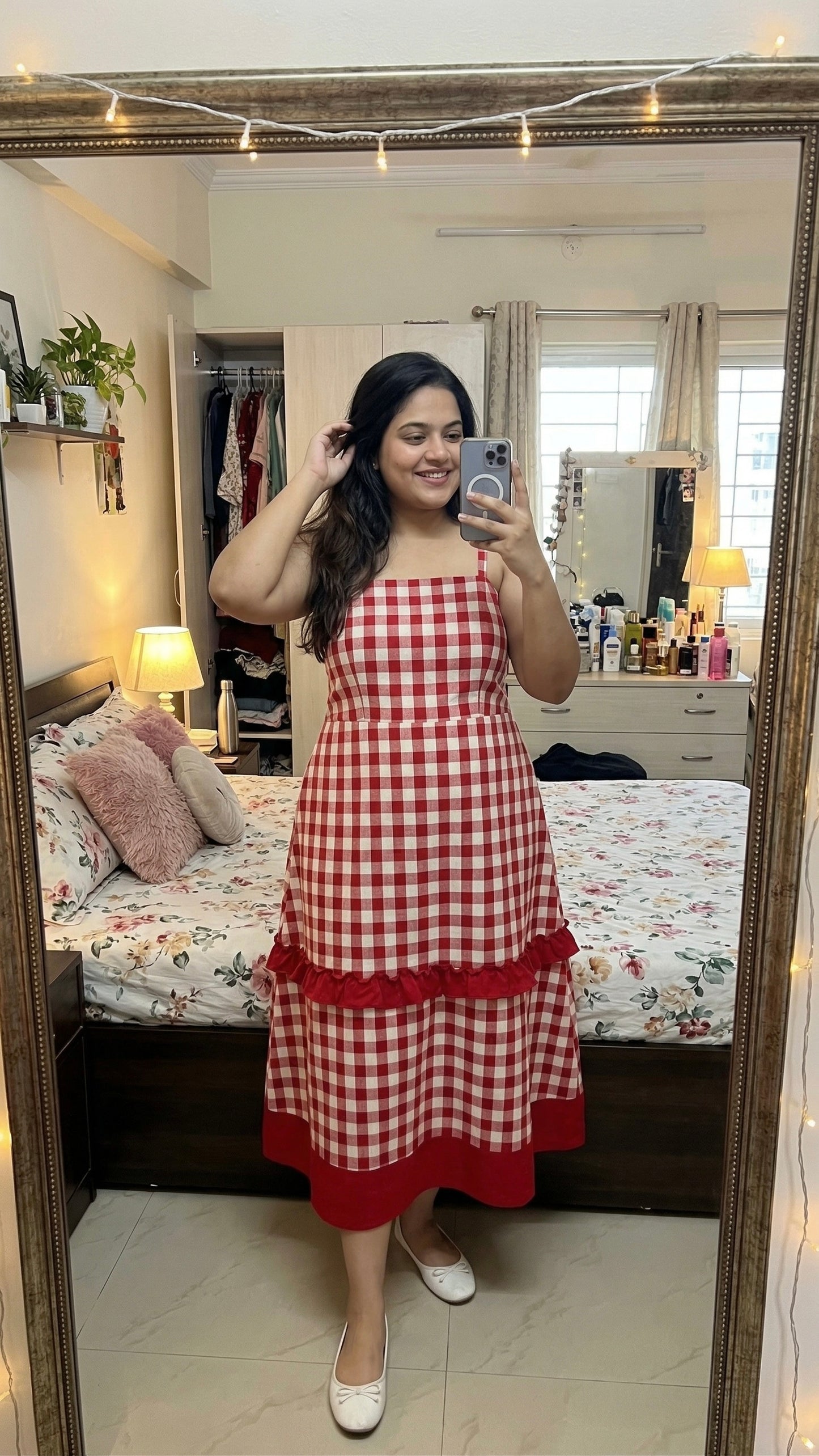 Woman taking a mirror selfie wearing a red and white checkered dress in a bedroom.