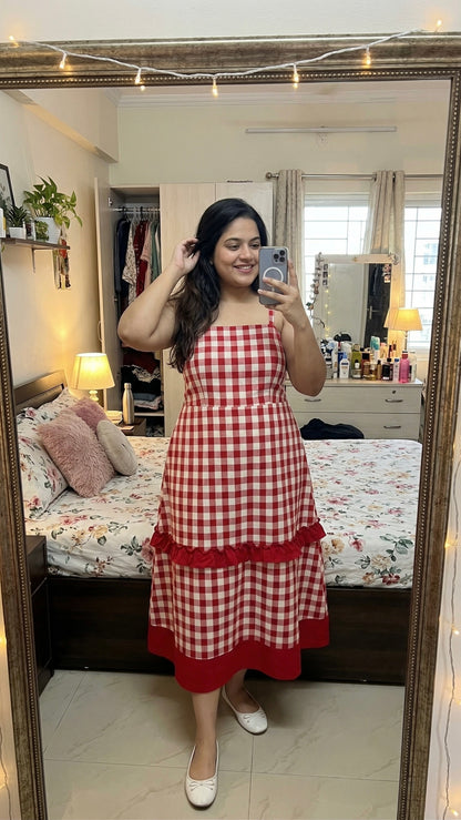 Woman taking a mirror selfie wearing a red and white checkered dress in a bedroom.