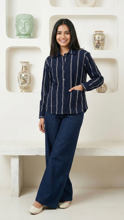 Woman wearing a navy striped shirt and dark pants standing in a decorative room.