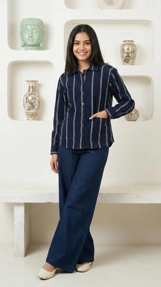 Woman wearing a navy striped shirt and dark pants standing in a decorative room.