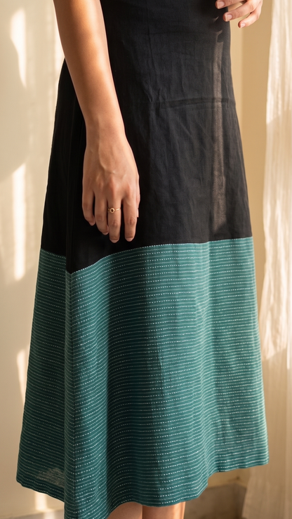 Person wearing a black and teal dress standing in a softly lit room.
