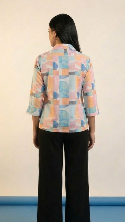 Person wearing a colorful geometric-patterned shirt and black pants on a plain background