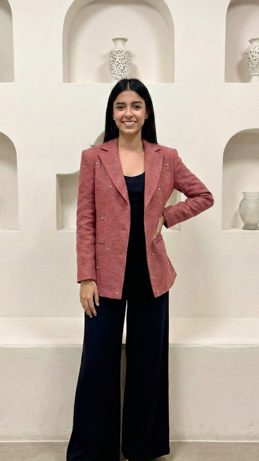 Woman wearing a pink blazer over a black top and wide-leg pants in a white room with shelves.