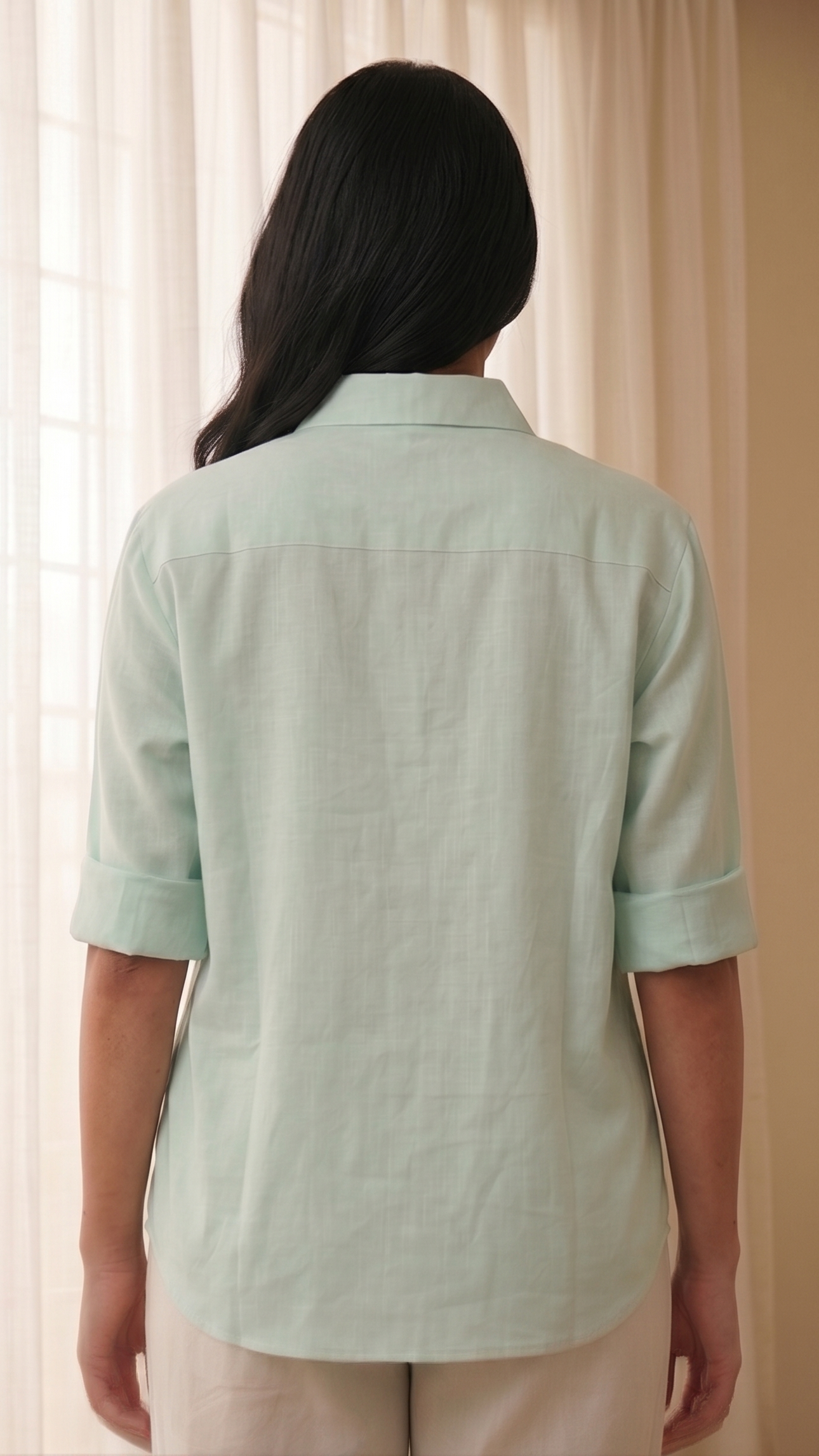 Person wearing a light green shirt standing in front of a beige curtain