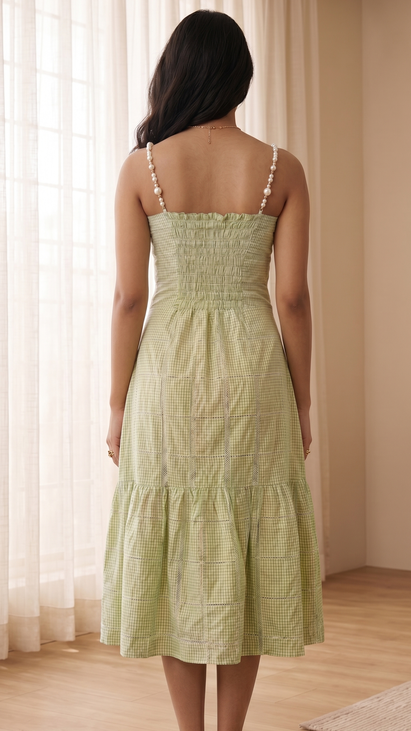 Woman wearing a light green dress standing in a room with curtains and wooden floor.