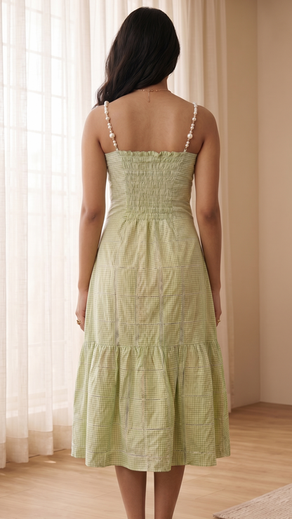 Woman wearing a light green dress standing in a room with curtains and wooden floor.