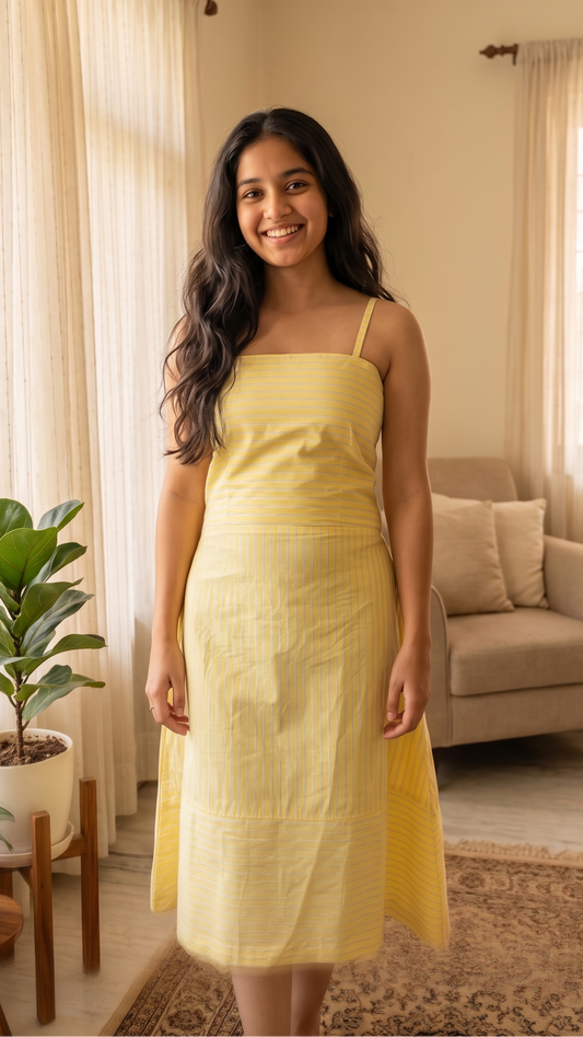 Woman in a yellow dress standing in a living room with plants and furniture.