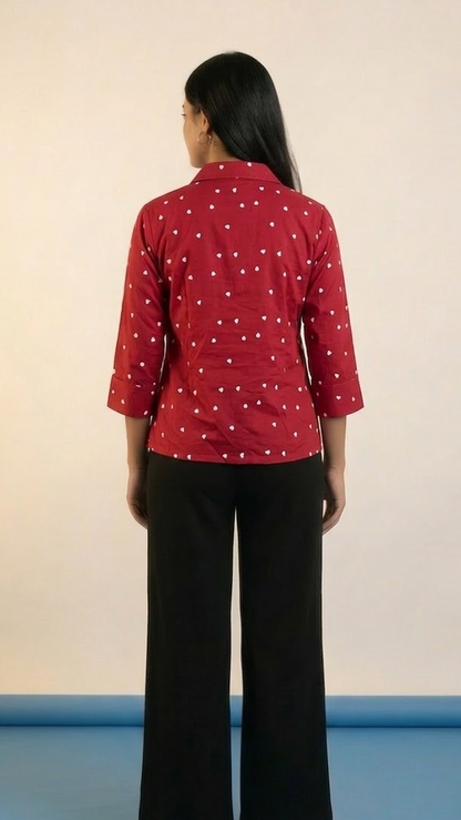 Person wearing a red patterned shirt and black pants on a plain background