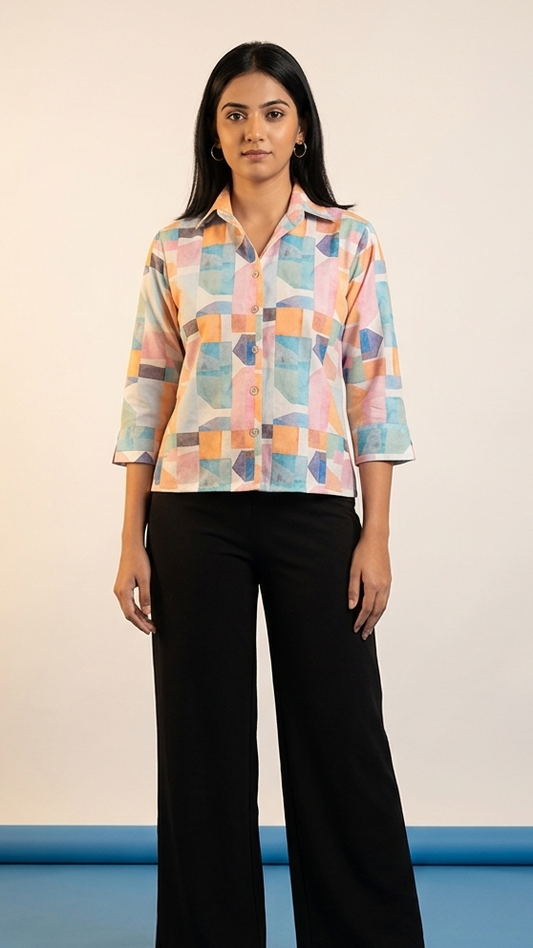 Woman wearing a colorful geometric-patterned shirt and black pants on a plain background