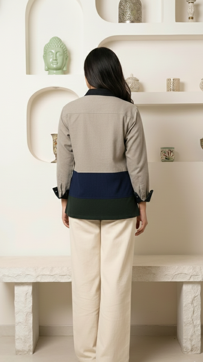 Person wearing a beige and navy top with white pants in a minimalistic room.