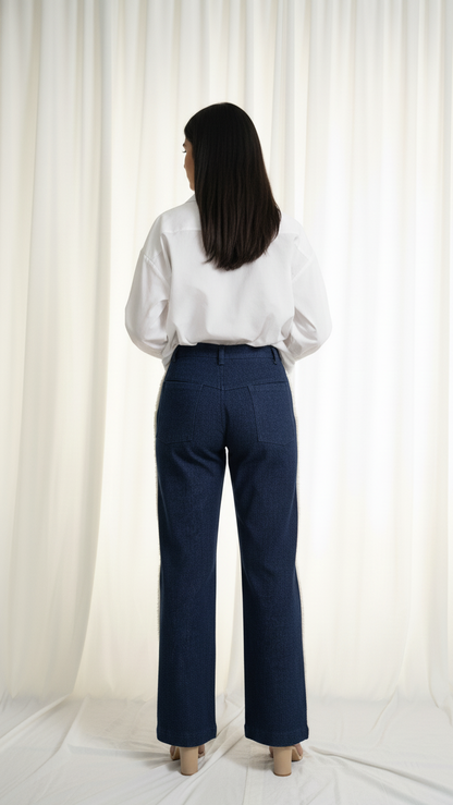 Person wearing a white blouse and navy pants standing against a white curtain.