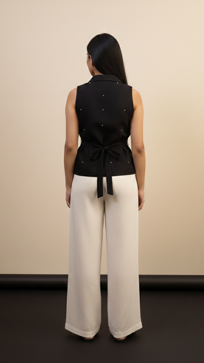 Person wearing a black sleeveless top and white pants against a beige wall.