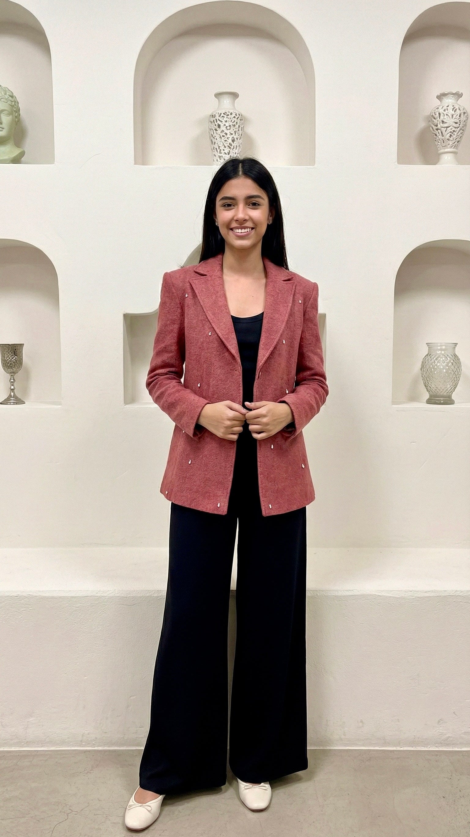 Woman wearing a pink blazer and black pants in a room with shelves displaying vases.