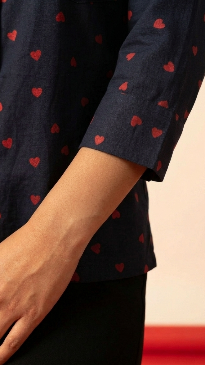 Navy blue shirt with red heart patterns worn by a person, on a plain background