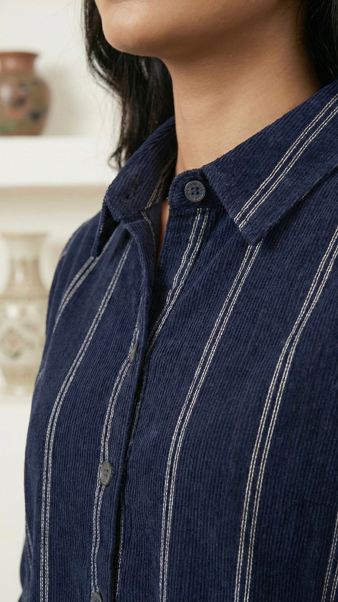 Close-up of a person wearing a navy blue shirt with white stripes, blurred background