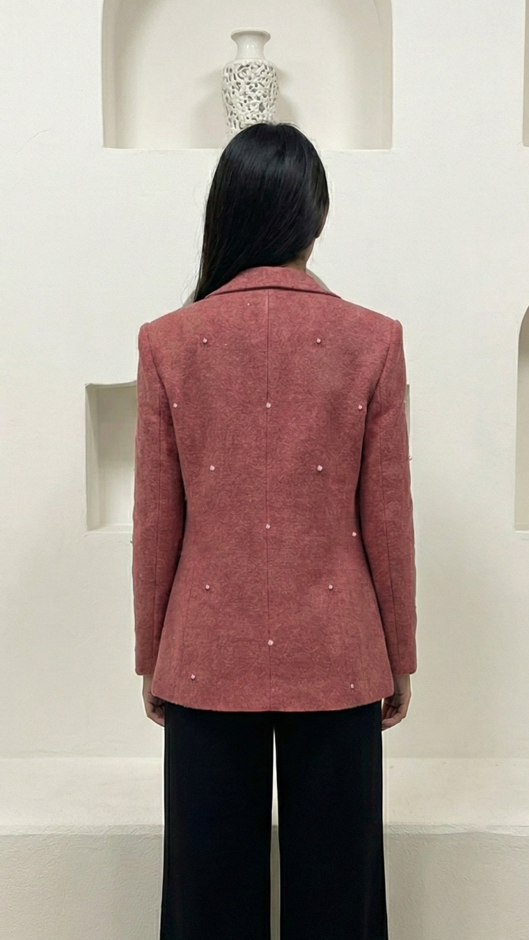 Person wearing a pink blazer in front of decorative shelves with vases.
