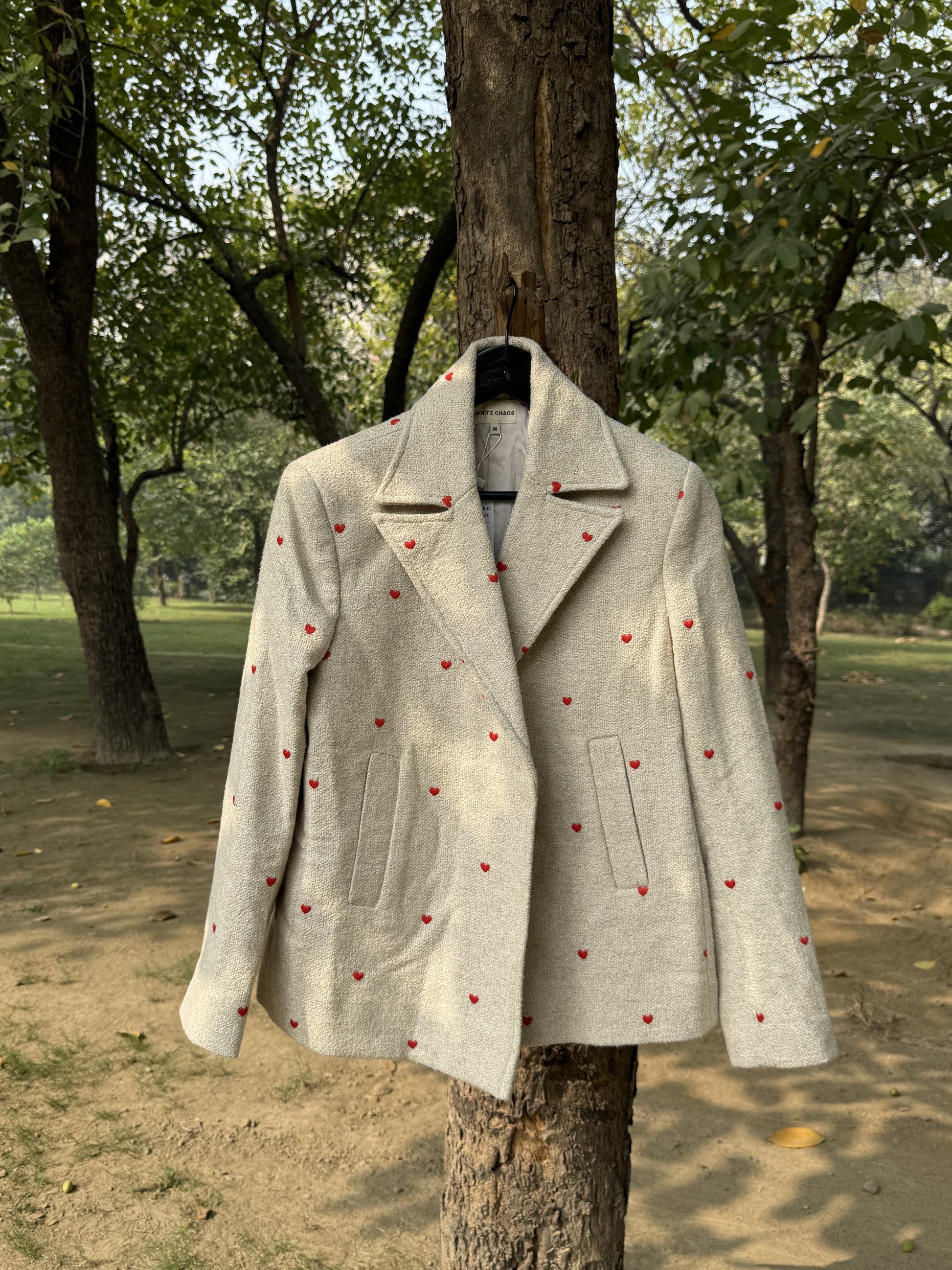 Light gray coat with red heart patterns hanging on a tree in a park setting
