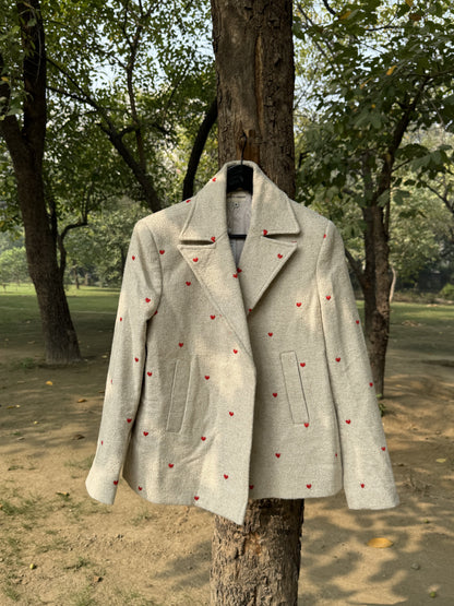 Light gray coat with red heart patterns hanging on a tree in a park setting