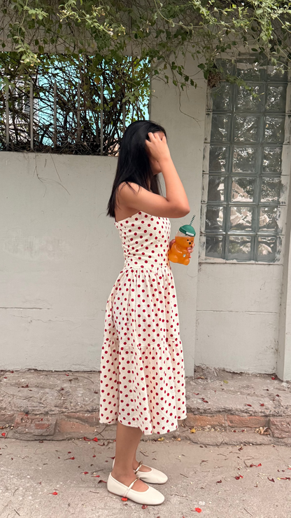 Woman in a white dress with red patterns standing outdoors near a building.