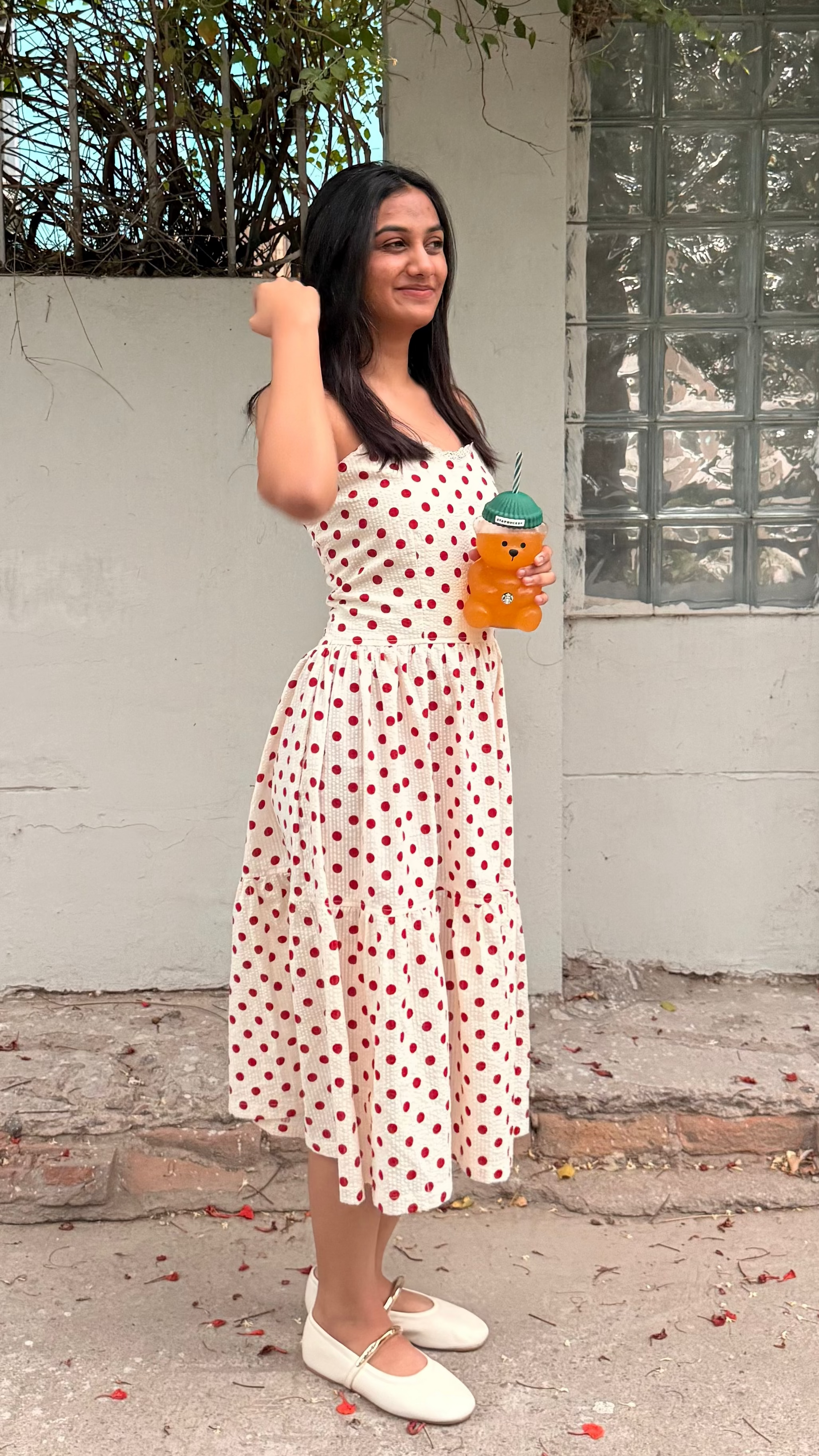 Woman in a polka dot dress holding a drink under a tree