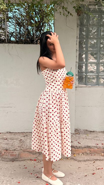 Woman in a white dress with red patterns standing outdoors, holding a drink.