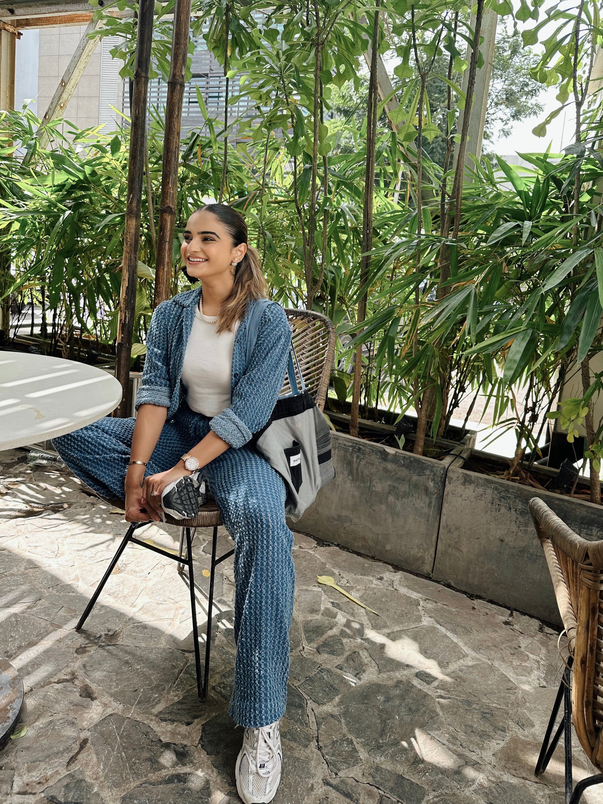 Woman sitting outdoors in a garden setting with greenery and stone pavement.
