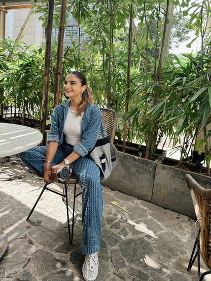 Woman sitting outdoors in a garden setting with greenery and stone pavement.