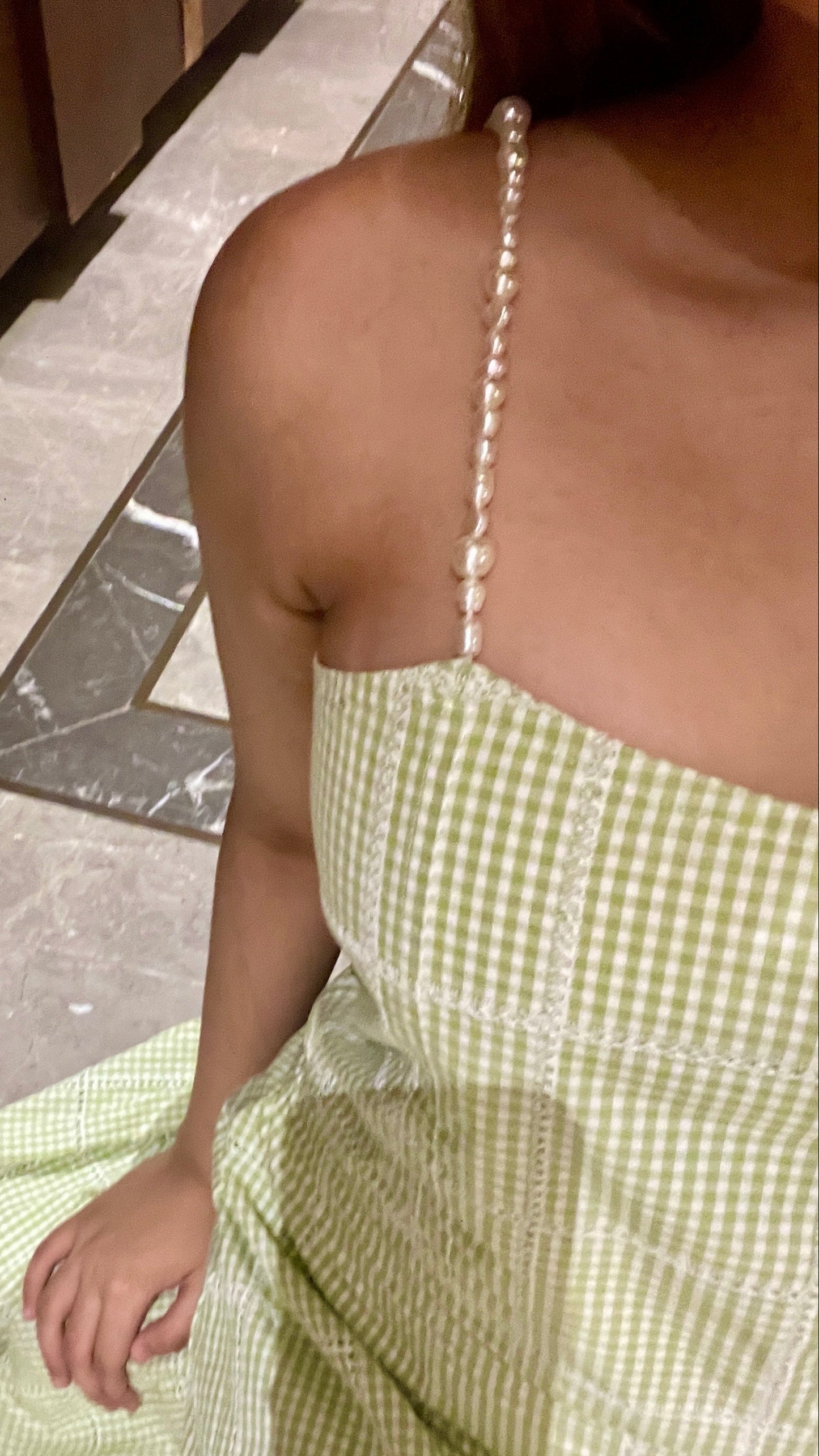 Person wearing a green checkered dress with pearl straps on a stone floor.