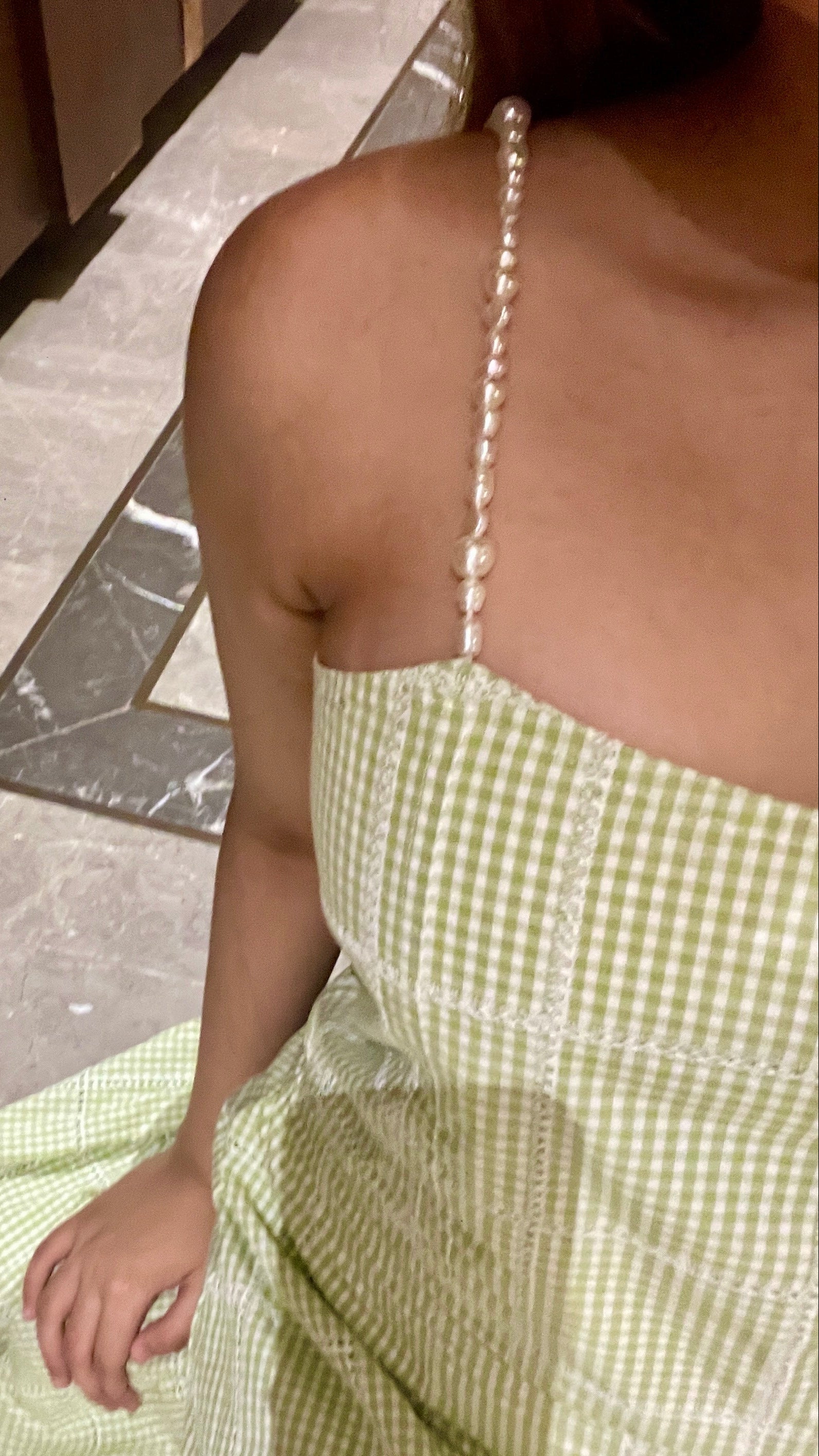 Person wearing a green checkered dress with pearl straps on a stone floor.