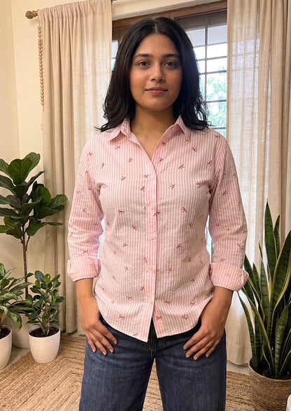 Woman wearing a pink patterned shirt standing in a room with plants and curtains.
