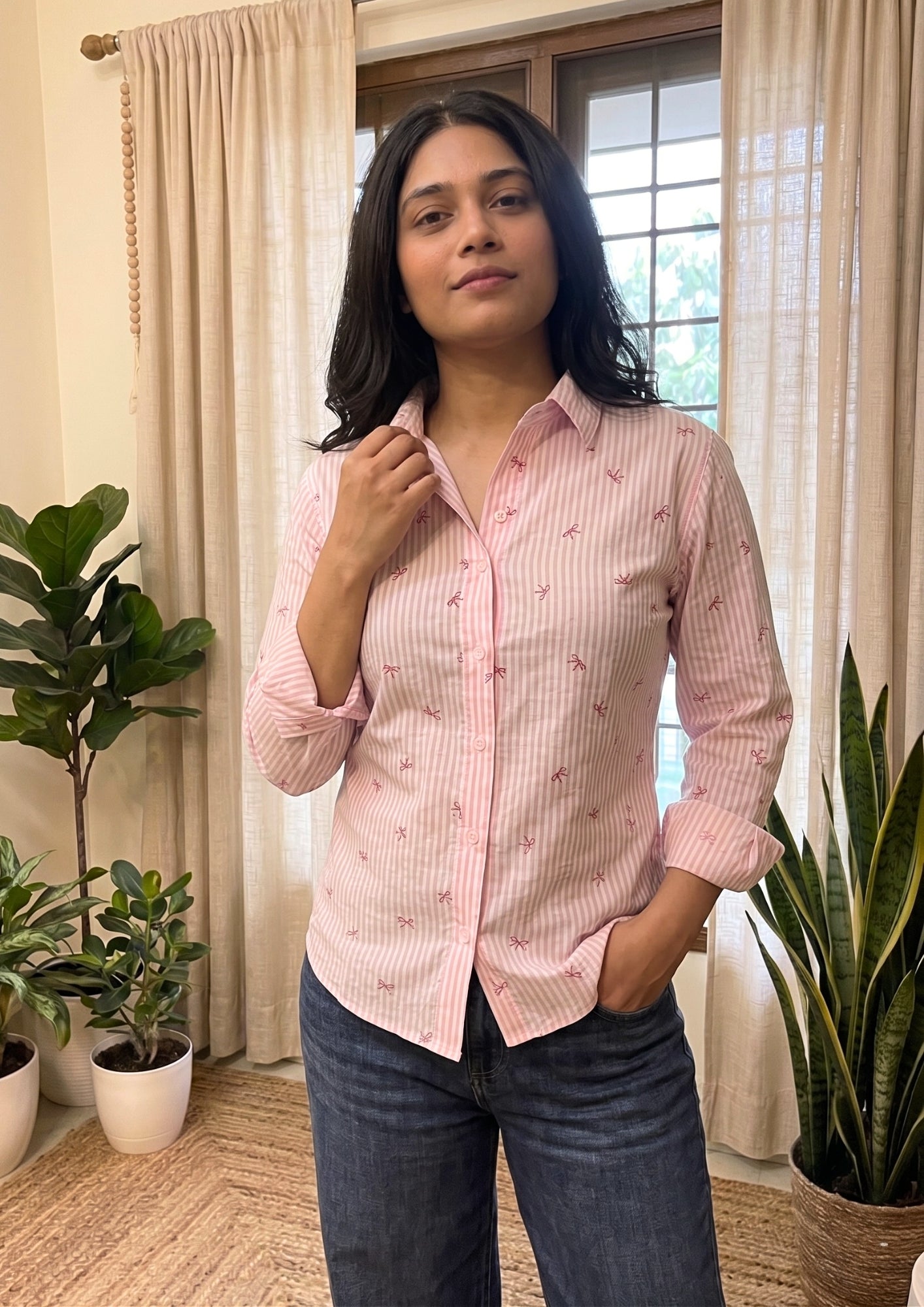 Woman wearing a pink checkered shirt in a room with plants and curtains
