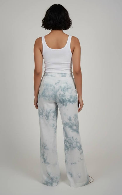 Person wearing a white tank top and light blue tie-dye pants on a plain background