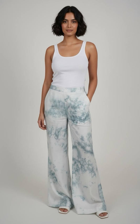 Woman wearing a white tank top and light blue tie-dye pants on a plain background