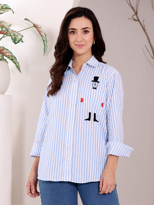Woman wearing a blue and white striped shirt with embroidered designs on a neutral background