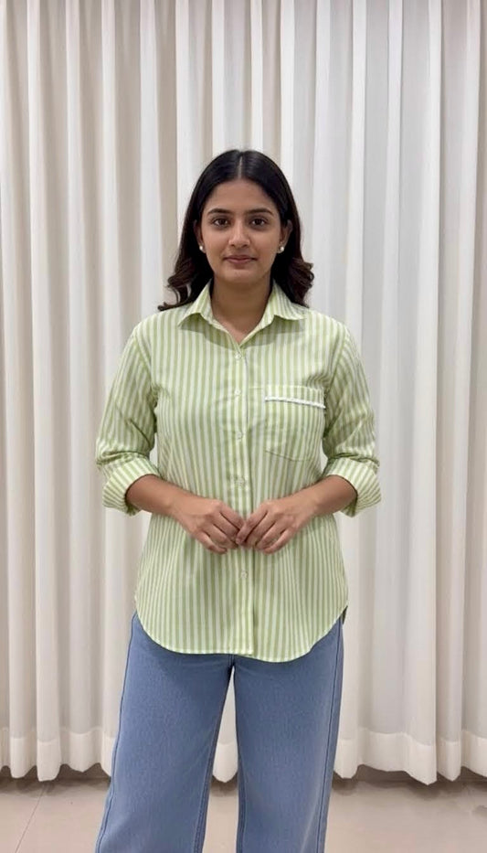 Woman wearing a light green striped shirt and blue pants standing against a white curtain background