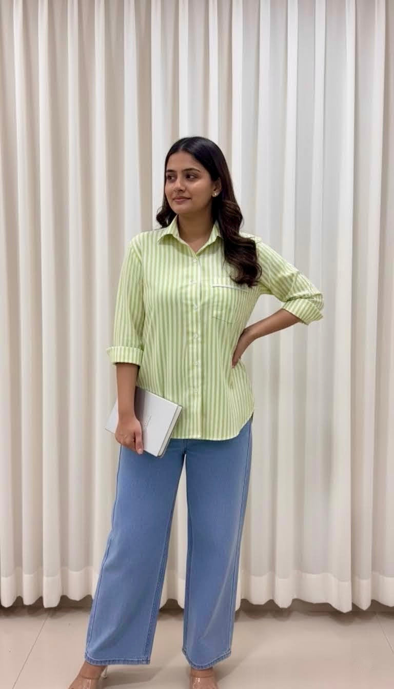 Woman wearing a green striped shirt and blue jeans standing against a white curtain background
